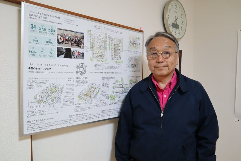 「希望のまち」の事業パネルの前に立つ奥田さん​