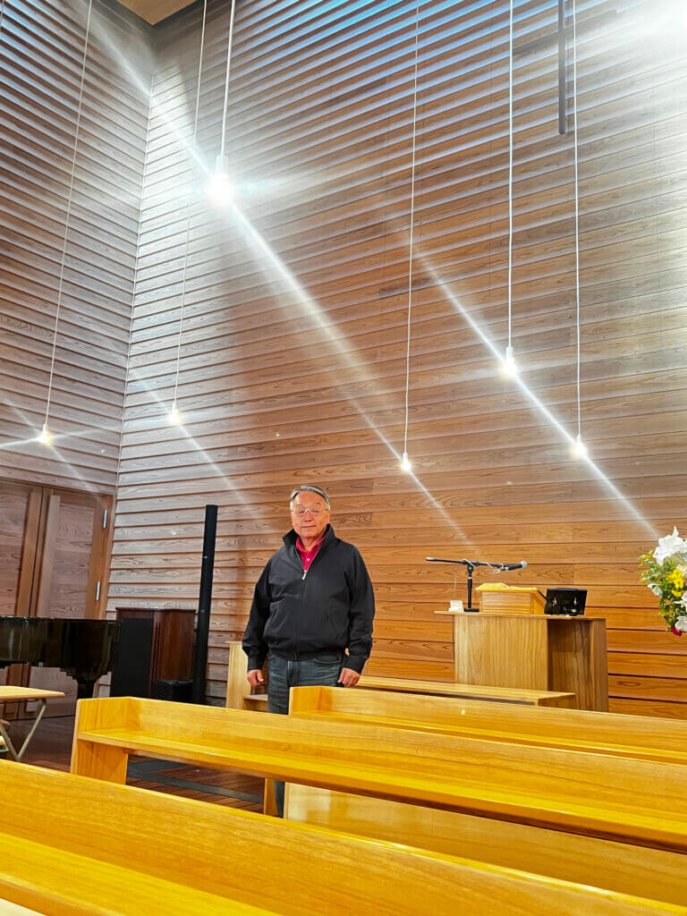 人々が出会う「軒の教会」と呼ばれる東八幡キリスト教会の礼拝堂。明るくまぶしい光と、その光を際立たせる影の中に立つ奥田さん